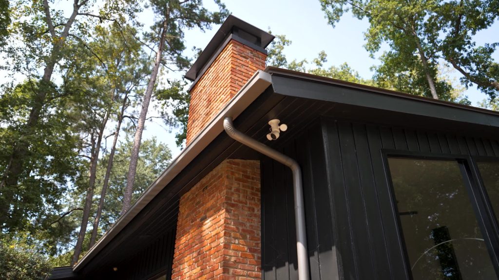 Box gutter and downspout on a dark board and batten home with a brick chimney