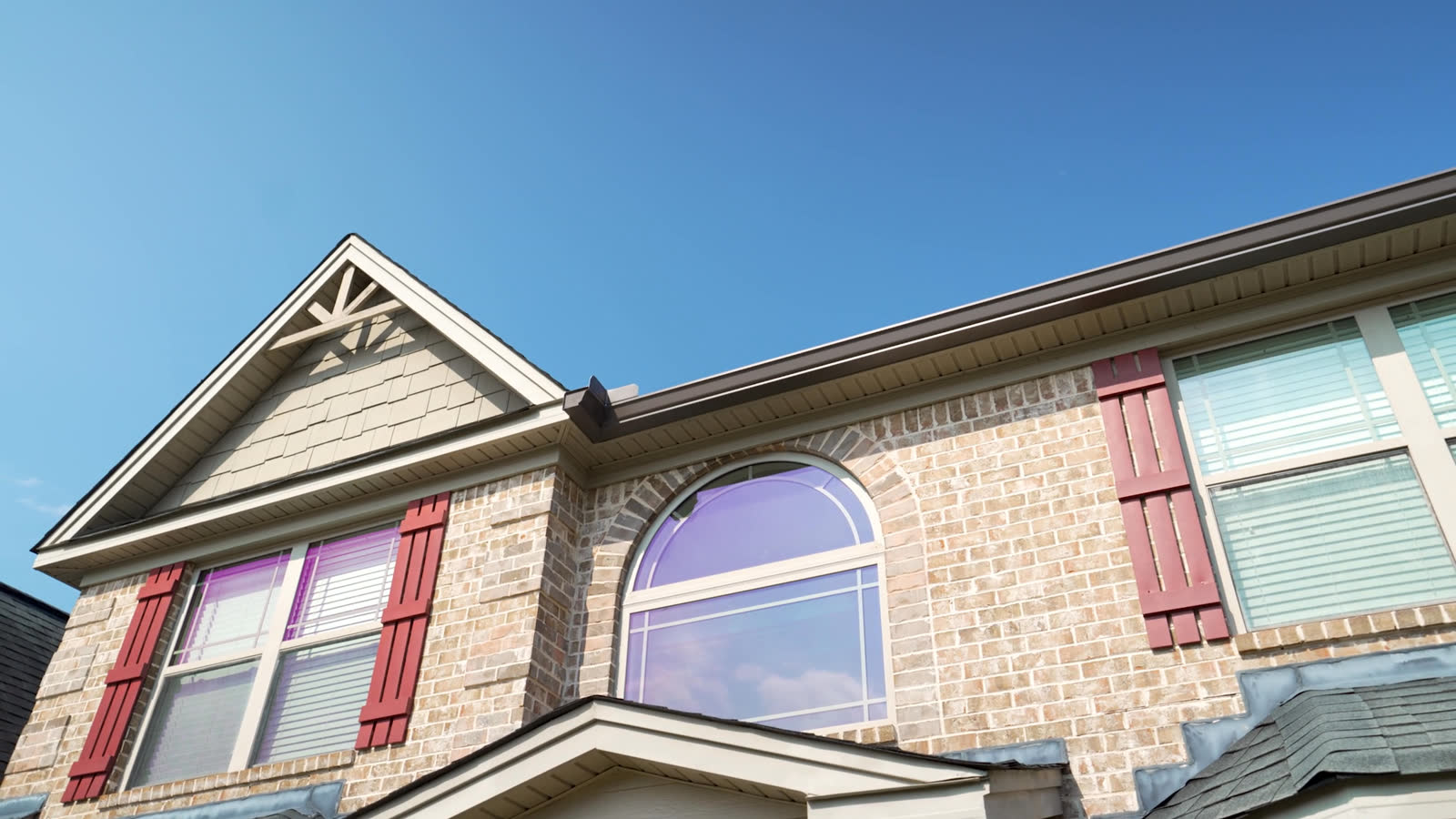 Brown seamless gutters on a brick home with a gabled roofline