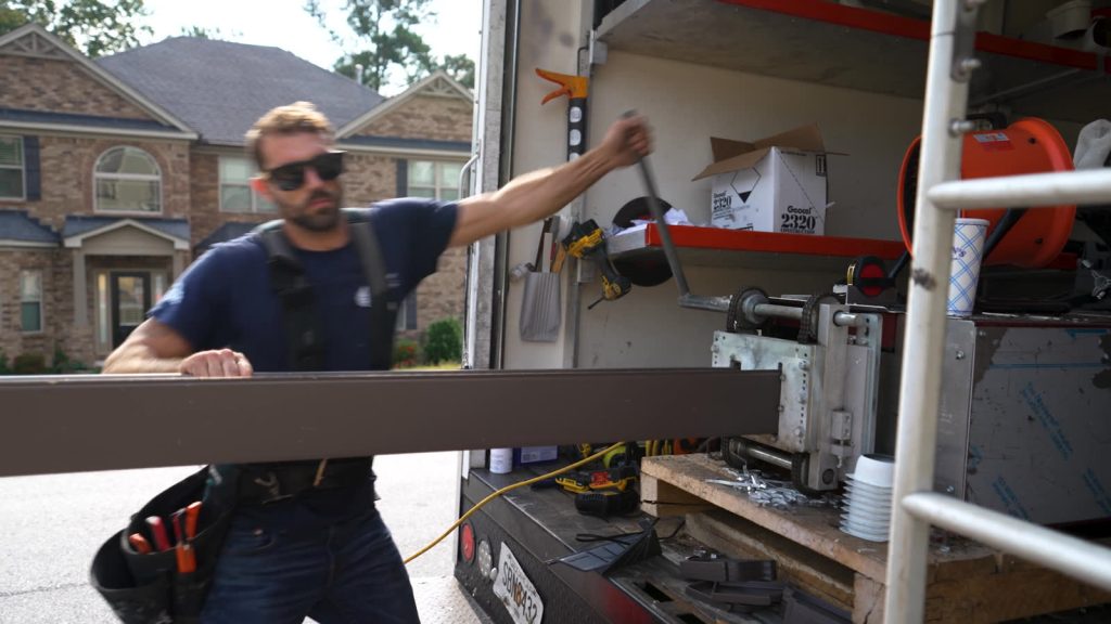Installer running a seamless brown gutter off the machine in the truck
