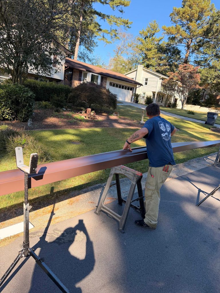 Installer checking a long brown gutter run on sawhorses at the curb in Smyrna