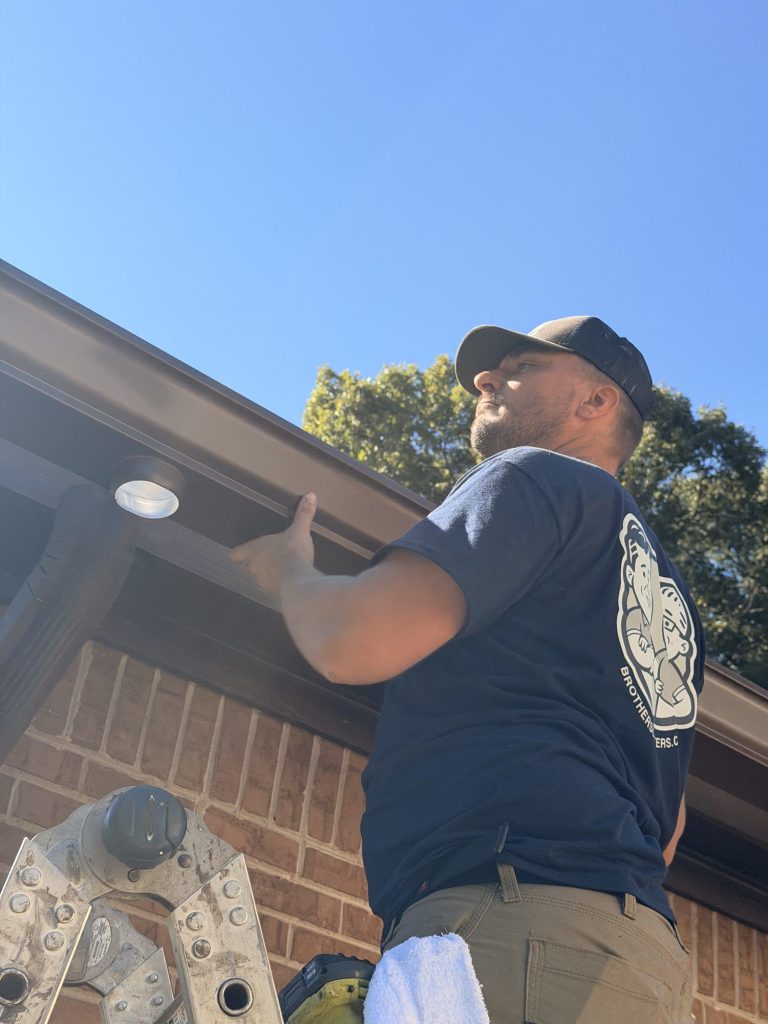 Installer checking a new brown gutter from below the eave in Smyrna