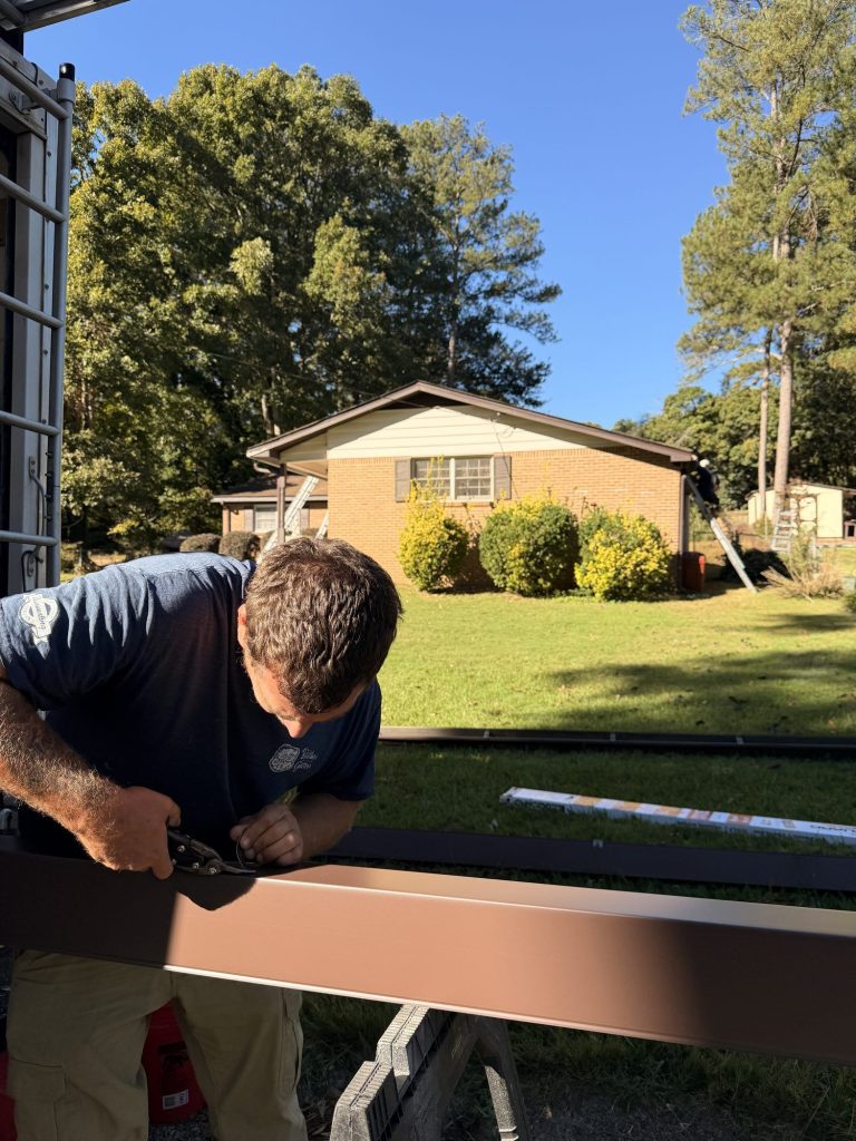 Installer cutting a brown gutter run to length on sawhorses in Smyrna