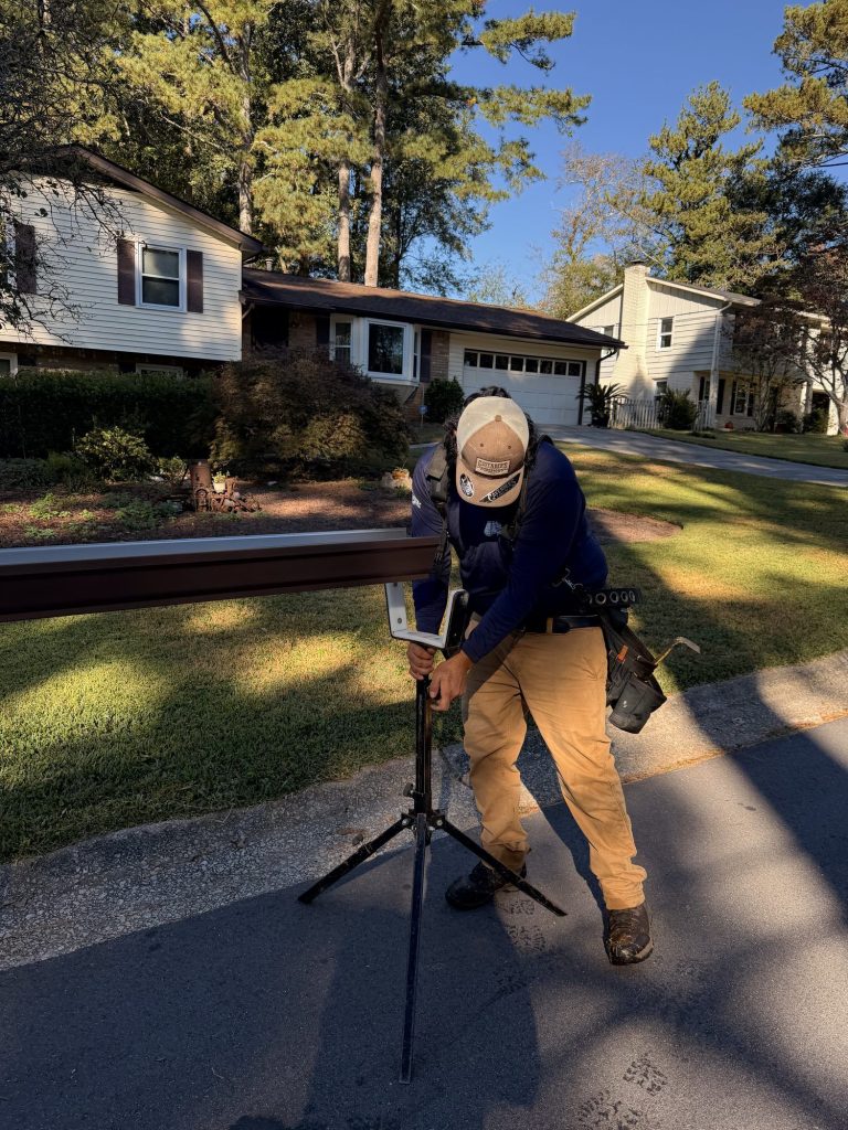 Installer measuring a brown seamless gutter run on a stand in the driveway in Smyrna