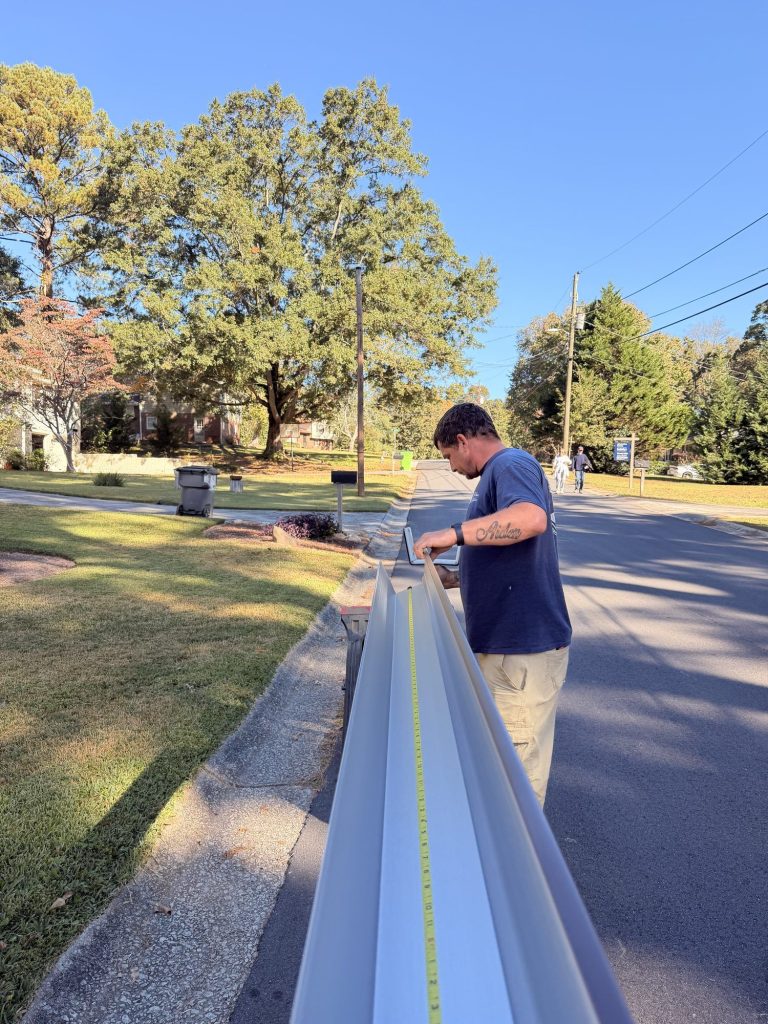 Installer measuring a long seamless gutter run laid out along the curb in Smyrna
