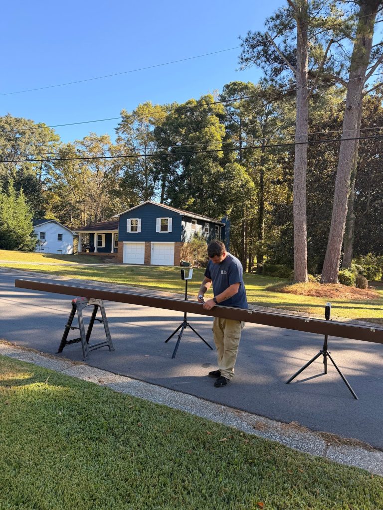 Installer measuring a seamless gutter run on stands in the street in Smyrna