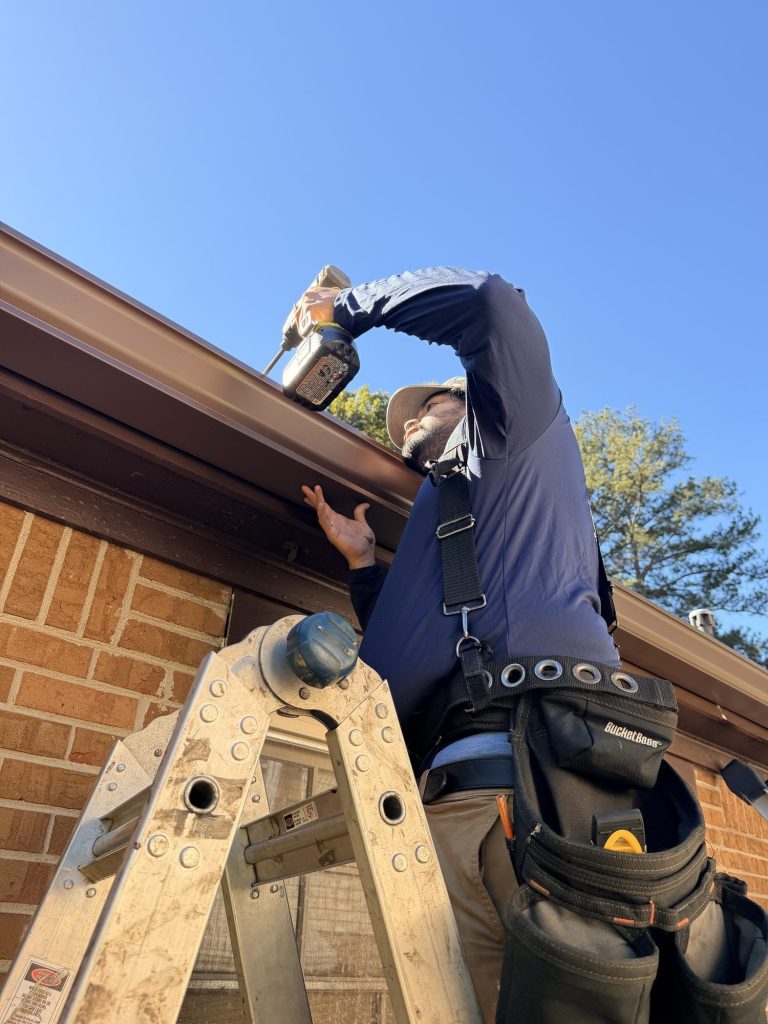 Installer on a ladder fastening hangers inside a brown gutter in Smyrna