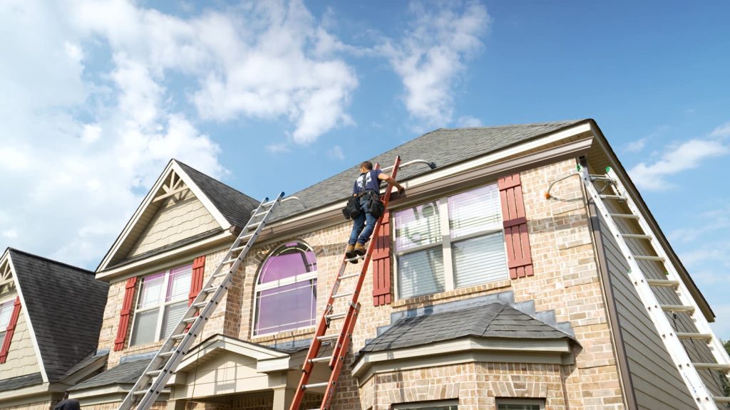 West Atlanta installer on a ladder hanging new gutters on a brick two story home