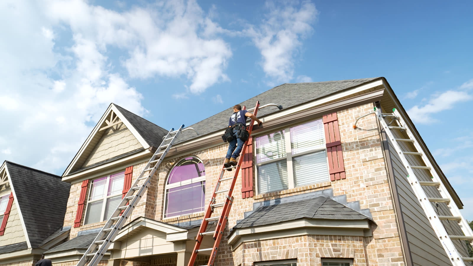 West Atlanta installer on a ladder hanging new gutters on a brick two story home