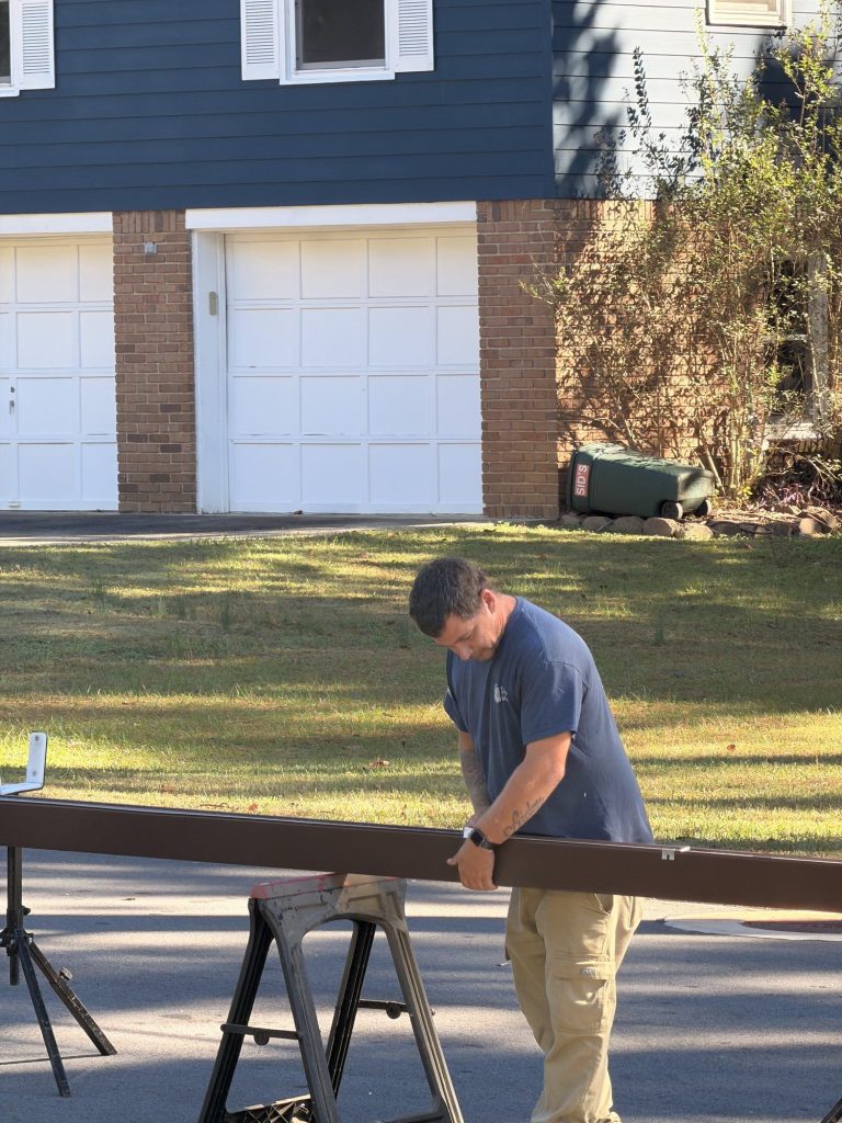 Installer prepping a brown gutter run on sawhorses in front of a brick home in Smyrna