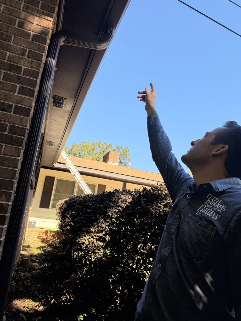 Brothers Gutters team member checking the new brown gutter at the roof edge in Smyrna
