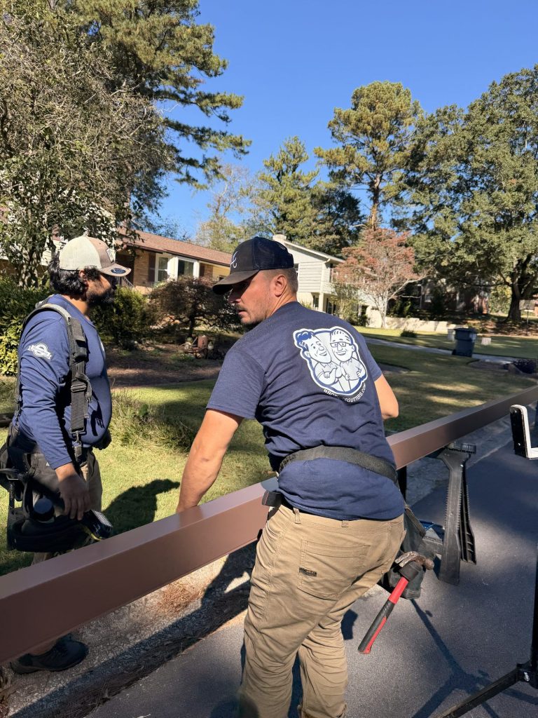 Two installers moving a long brown gutter run off the stands in Smyrna